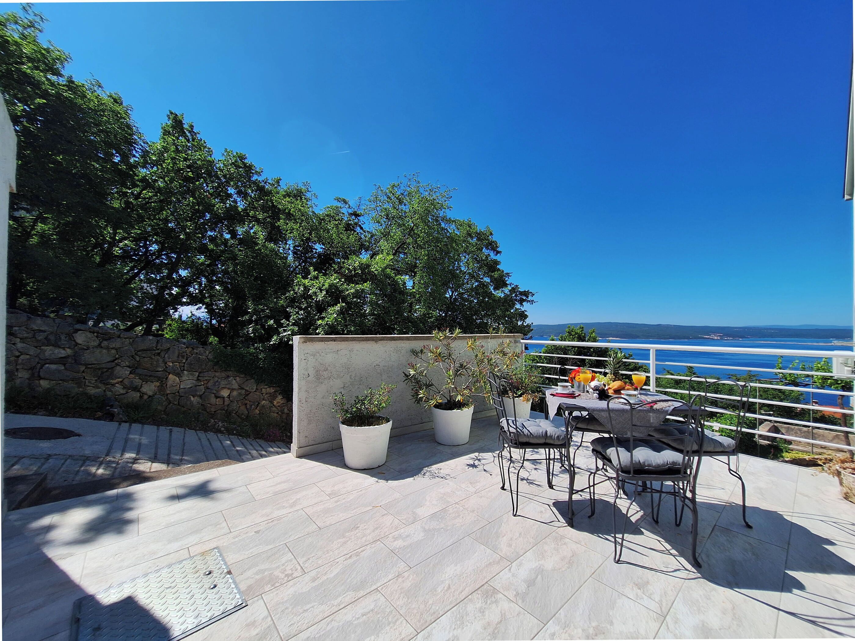 Eine Terrasse mit Tisch und Stühlen, Blumentöpfen und Blick auf das Meer.