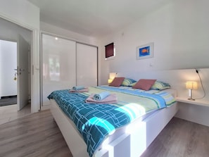Ein Schlafzimmer mit einem Bett, Nachttischen, einer Tür und einer Wand mit einem Bild.