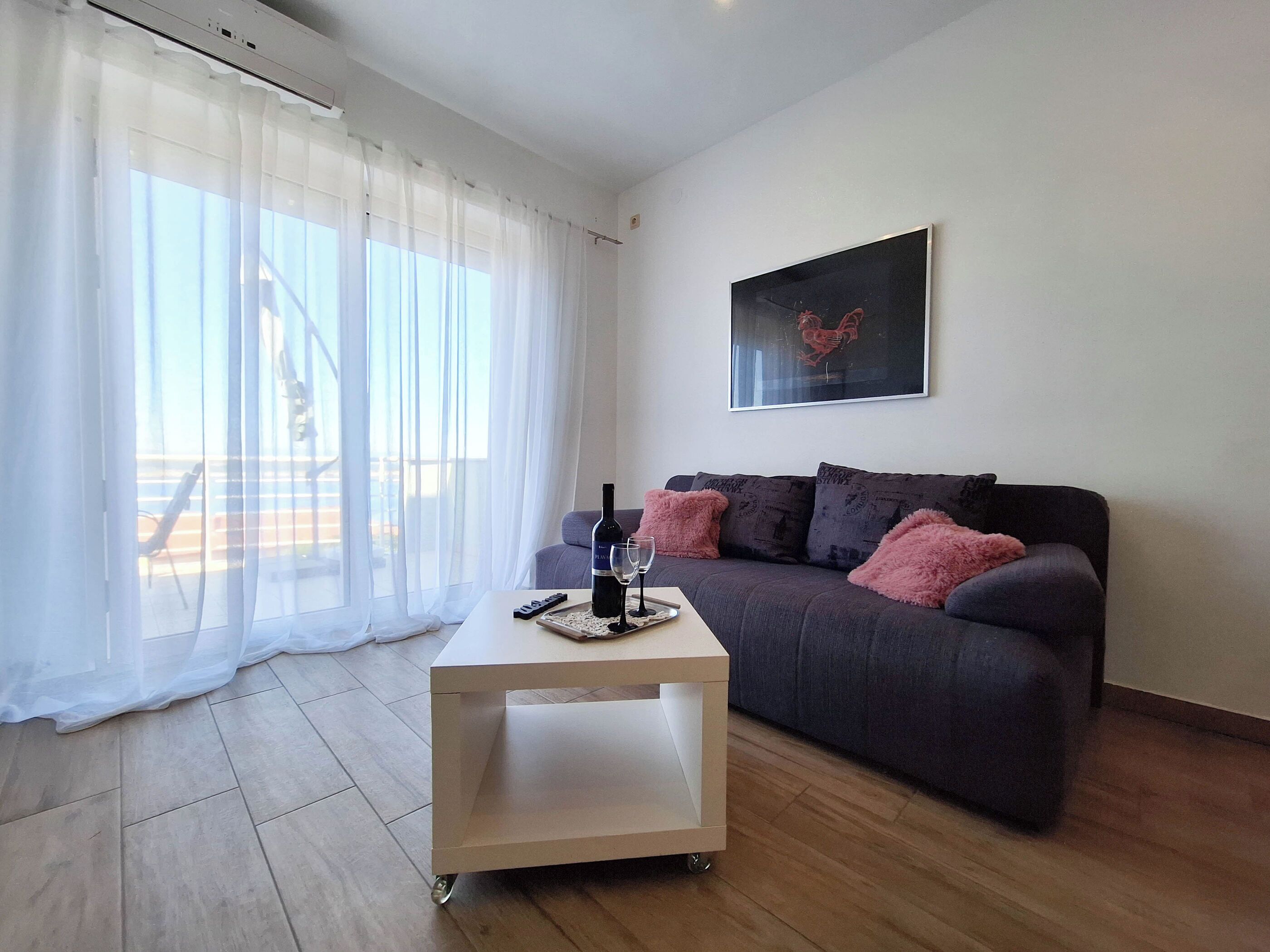 Una sala moderna con un sofá gris, una mesita de centro blanca y una botella de vino.