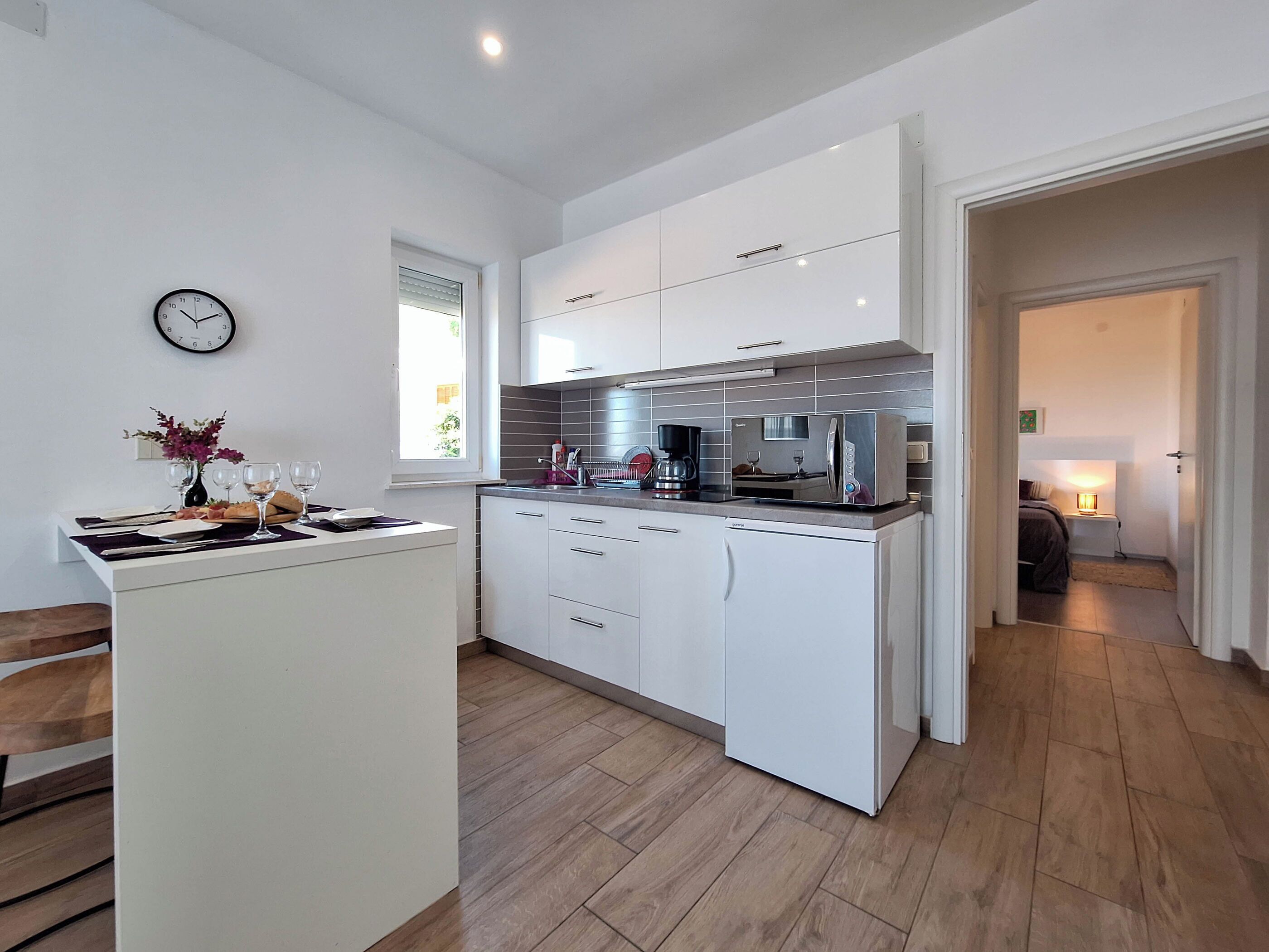 A modern kitchen with white cabinets, a built-in oven, and a dining area with a bench and table set for two.