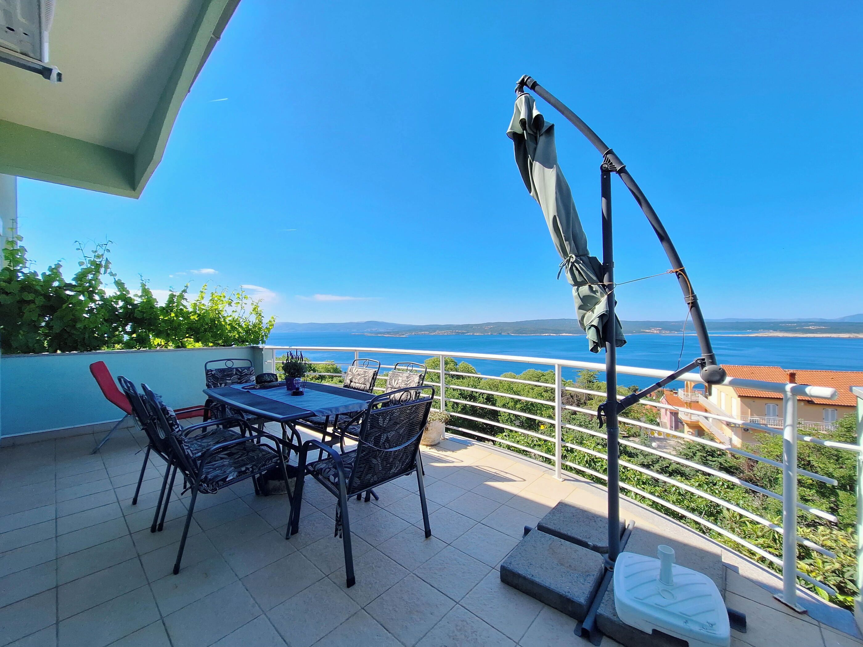 Una terraza con una mesa, sillas, una sombrilla metálica y vista al mar.