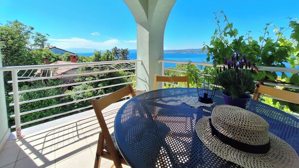 Een balkon met een tafel en stoelen, met uitzicht op een prachtig zeegezicht en groen.