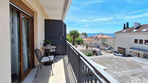A balcony with a table and chairs, a potted plant, and a view of the sea and neighboring buildings. - Apartment and Rooms Katunar (Crikvenica)