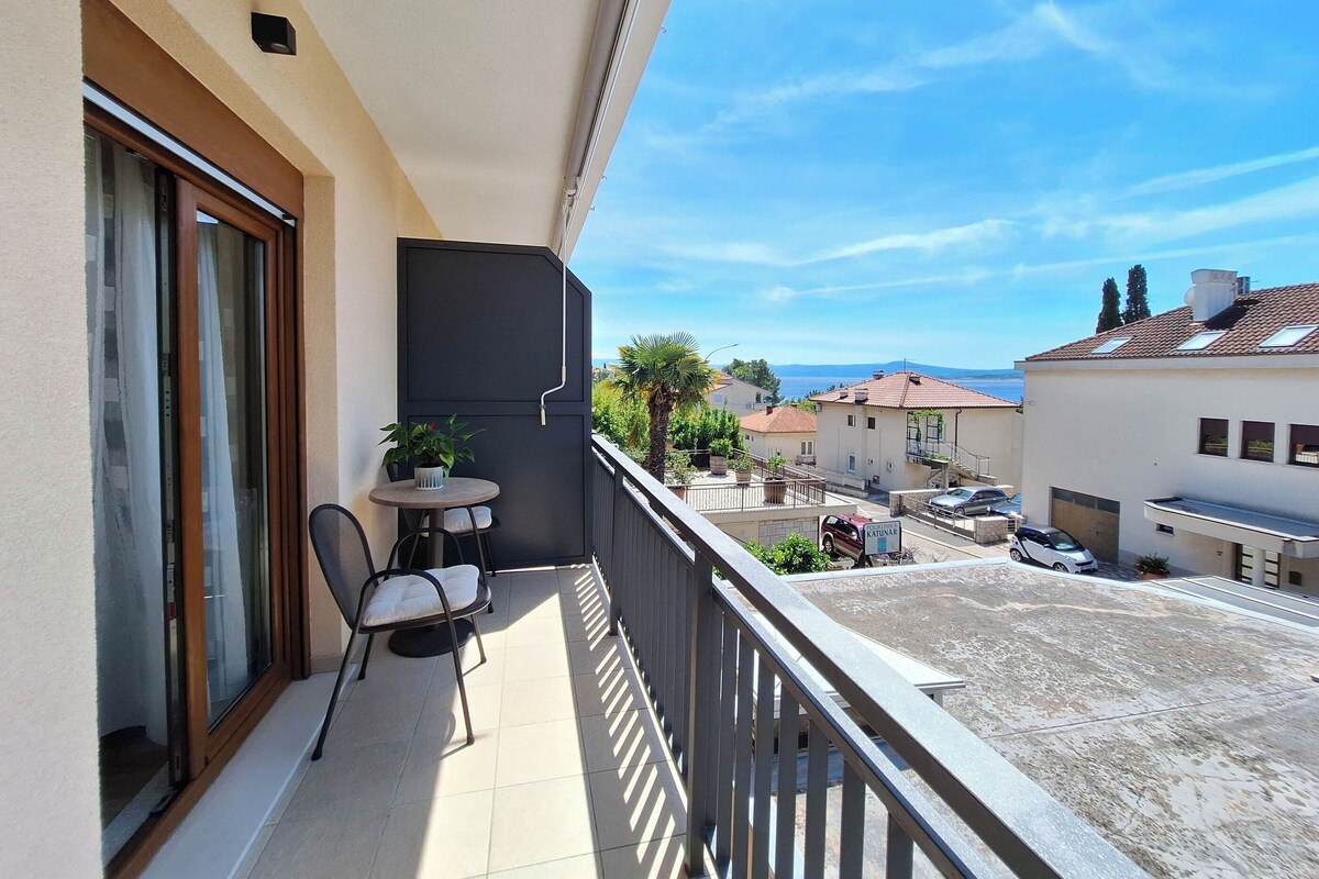 Un balcon avec une table et des chaises, un pot de fleurs et une vue sur la mer et les bâtiments voisins.