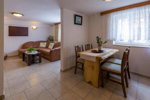 A living room with a sofa, a small table with a plant, and a dining area with a wooden table and chairs. - Apartments Panos (Novi Vinodolski)