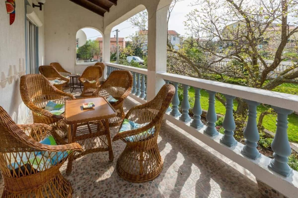 A covered outdoor seating area with wicker furniture and a view of the garden.