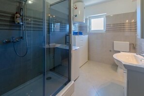A modern bathroom with a glass shower enclosure, a white sink, and a small window. - Apartments Panos (Novi Vinodolski)