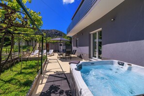 Un espace piscine extérieur moderne, doté d’un jacuzzi, de chaises longues et d’une pergola couverte de plantes grimpantes.