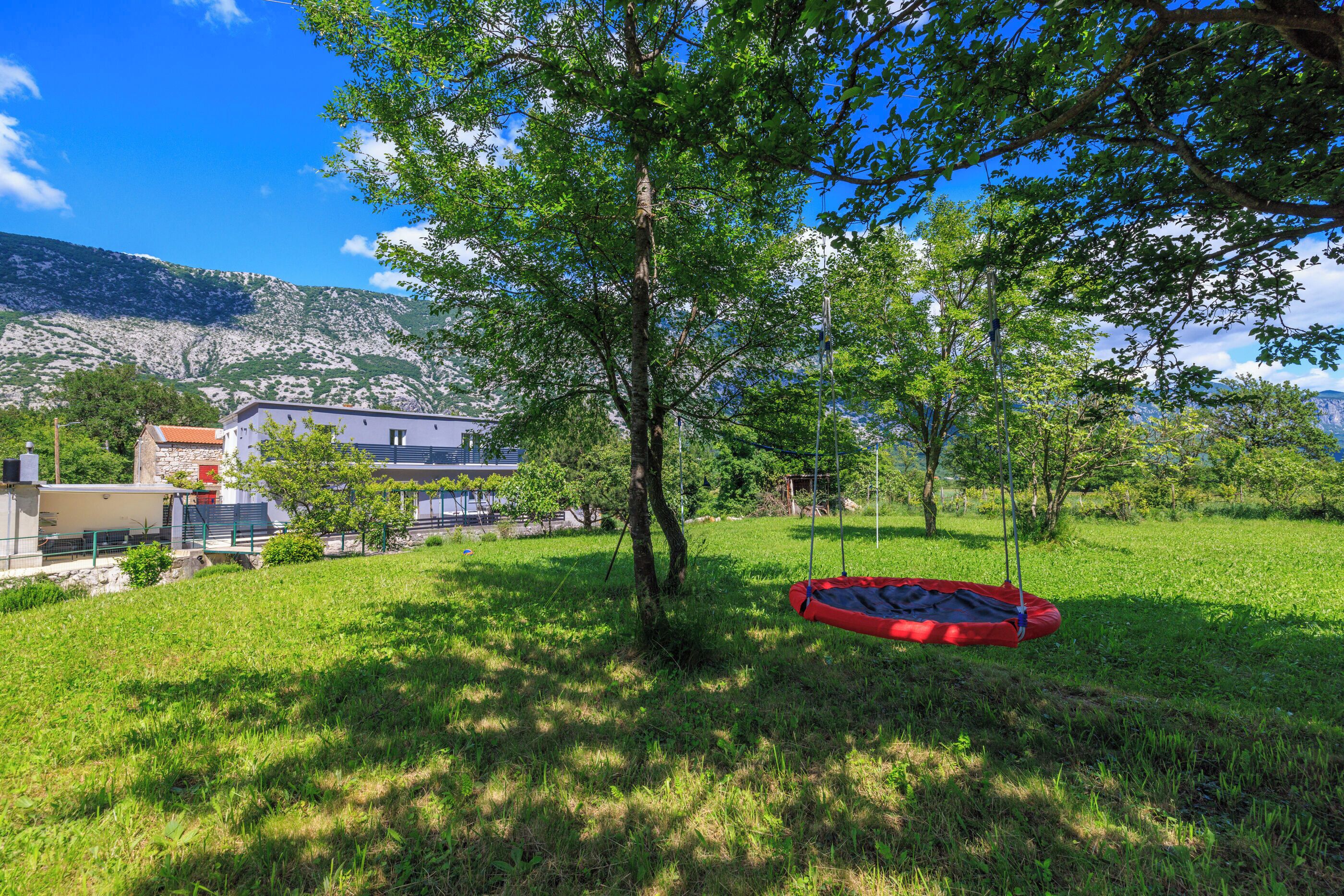A grassy area with a red swing set and a tree in the center.