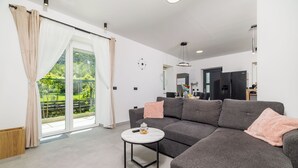 Una sala de estar moderna con un sofá gris, una mesita redonda y un ventanal corredera que da a un balcón.