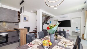 Un comedor moderno con una mesa dispuesta, un ramo de flores y una cocina al fondo.