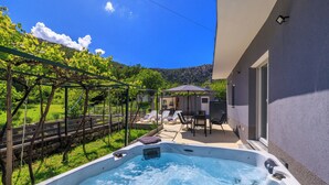 Un jacuzzi con pared de piedra y una pérgola cubierta de hiedra.