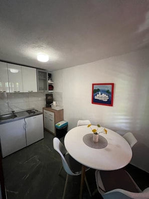 A compact kitchen with white cabinets, a sink, and a small dining area with a table and chairs. - Apartments Luna (Marina)