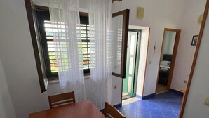 A dining area with a wooden table, chairs, a window with curtains, and a blue tiled floor. - Apartments Luna (Marina)