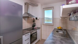 Ett kompakt kök med ett kylskåp, en ugn och en diskho i rostfritt stål. Ett fönster ger utsikt över omgivningen.