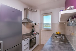 Eine kleine Küche mit einem Edelstahl-Kühlschrank, Backofen und Spüle. Ein Fenster bietet Blick ins Freie.