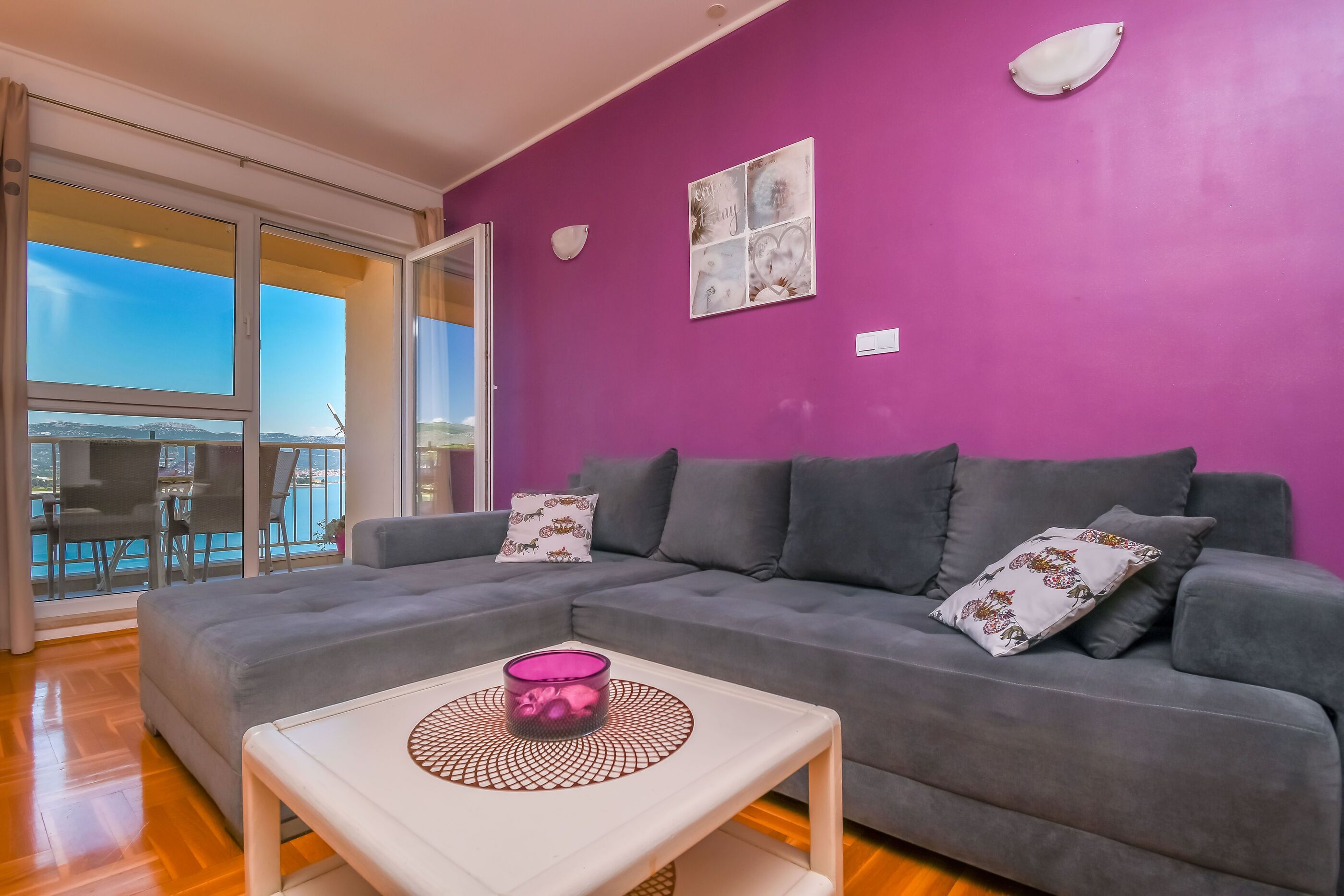 Una sala de estar con un sofá gris, una mesa de centro blanca y una pared morada.