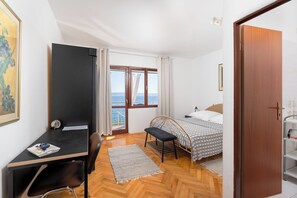 A bedroom with a bed, a desk, a chair, a window with a view of the sea, and a door. - Apartment Porat (Starigrad)