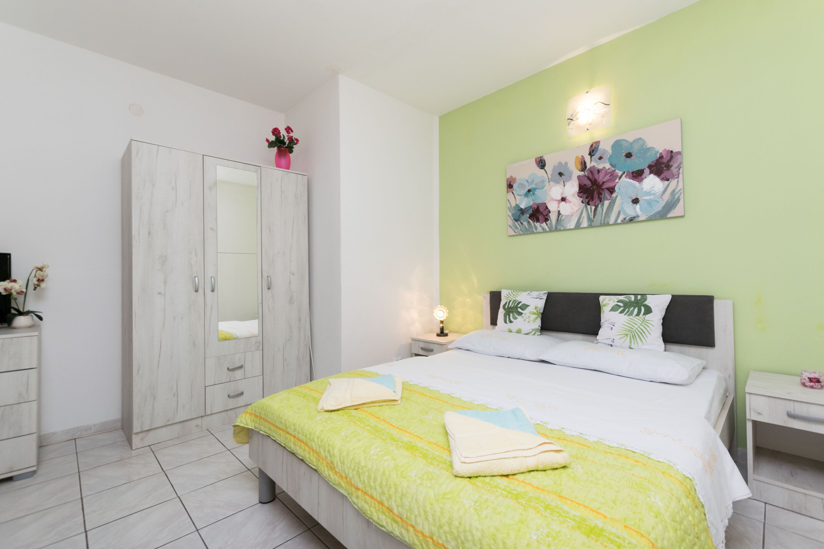 A bedroom with a bed, a wardrobe, a nightstand, and a wall-mounted light fixture.