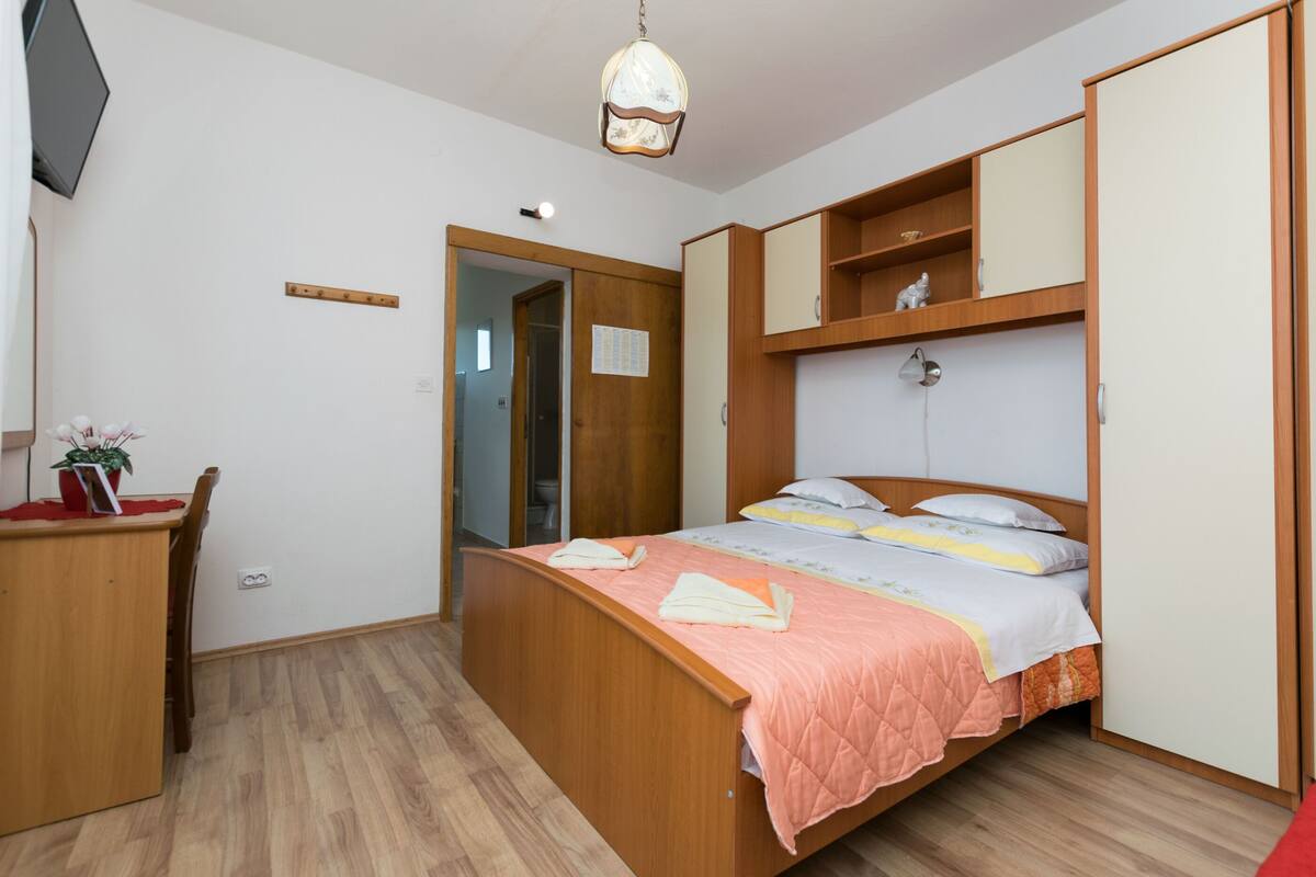Une chambre à coucher comprenant un lit, un bureau, une chaise, une armoire et un luminaire suspendu.