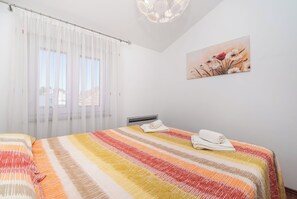 Une chambre d’hôtel avec un grand lit, une tête de lit, une fenêtre avec des rideaux légers et un tableau accroché au mur.