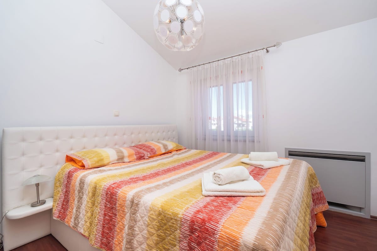 A neatly made bed with a striped blanket, a white headboard, and a bedside lamp.