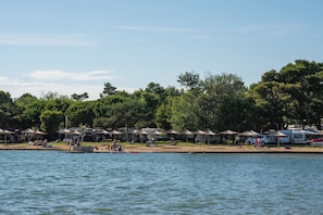 Un terrain de camping au bord d’un lac, avec plusieurs tentes et un bateau amarré sur la rive.