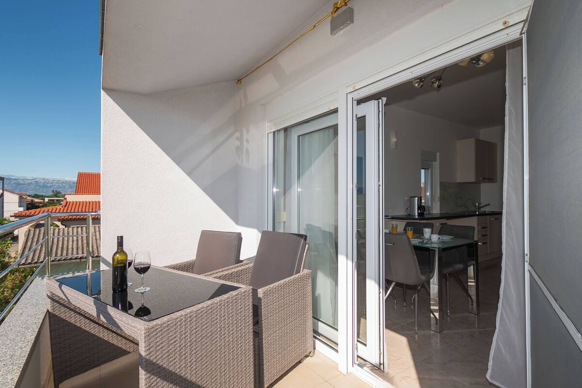 A balcony with wicker furniture, a glass table, and a bottle of wine.