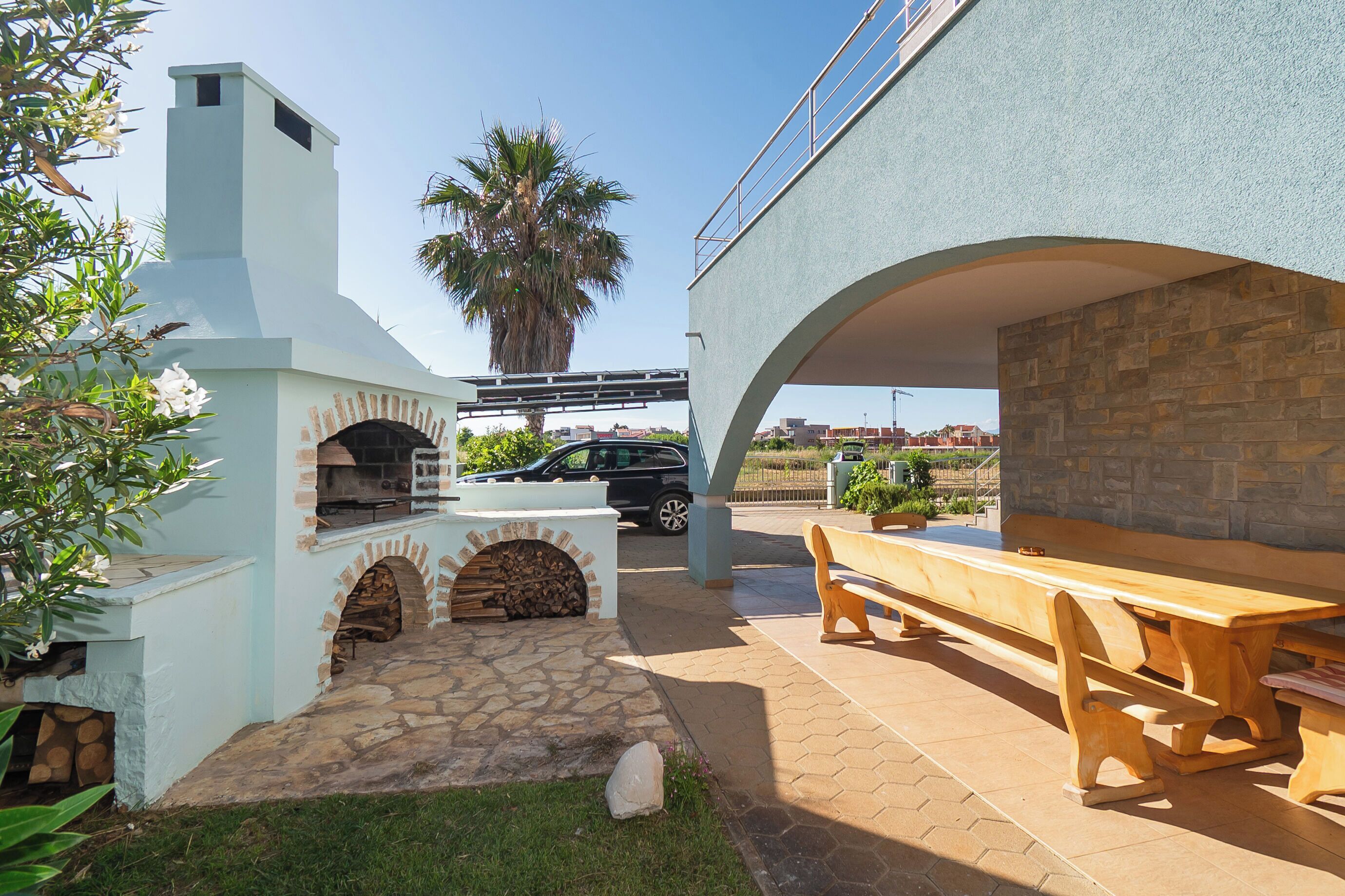 An outdoor patio with a stone fireplace, a wooden bench, and a car parked nearby.
