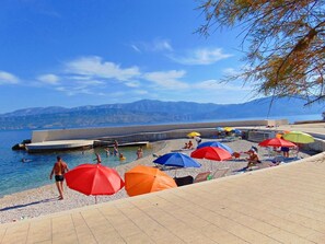 A beach with clear blue water, people swimming and sunbathing, and colorful umbrellas. - Apartment Tonci (Postira)