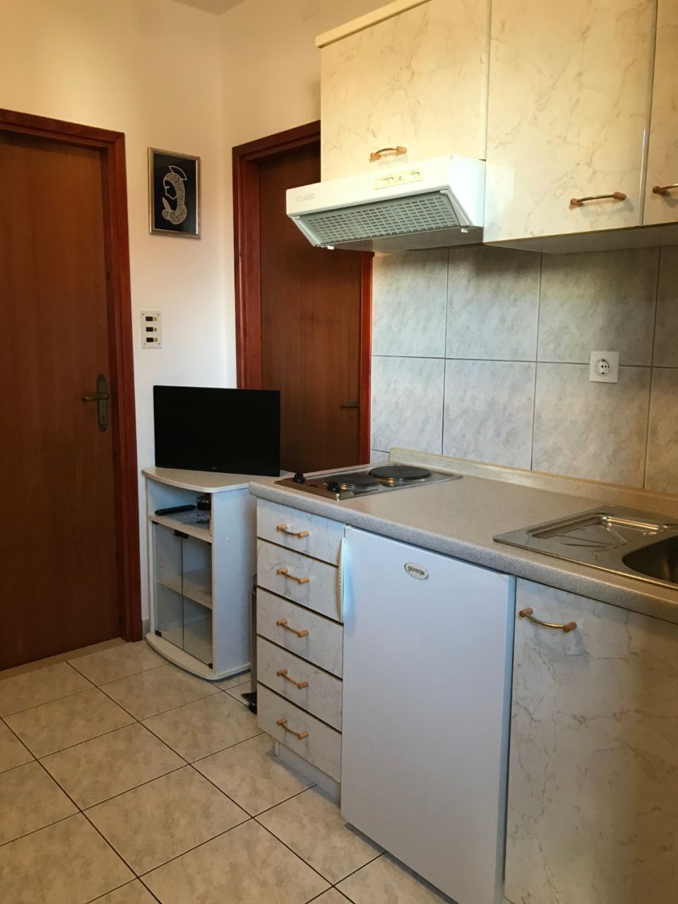 A compact kitchen with a built-in stove, a microwave, and a sink. There are cabinets with wooden handles and a small refrigerator.