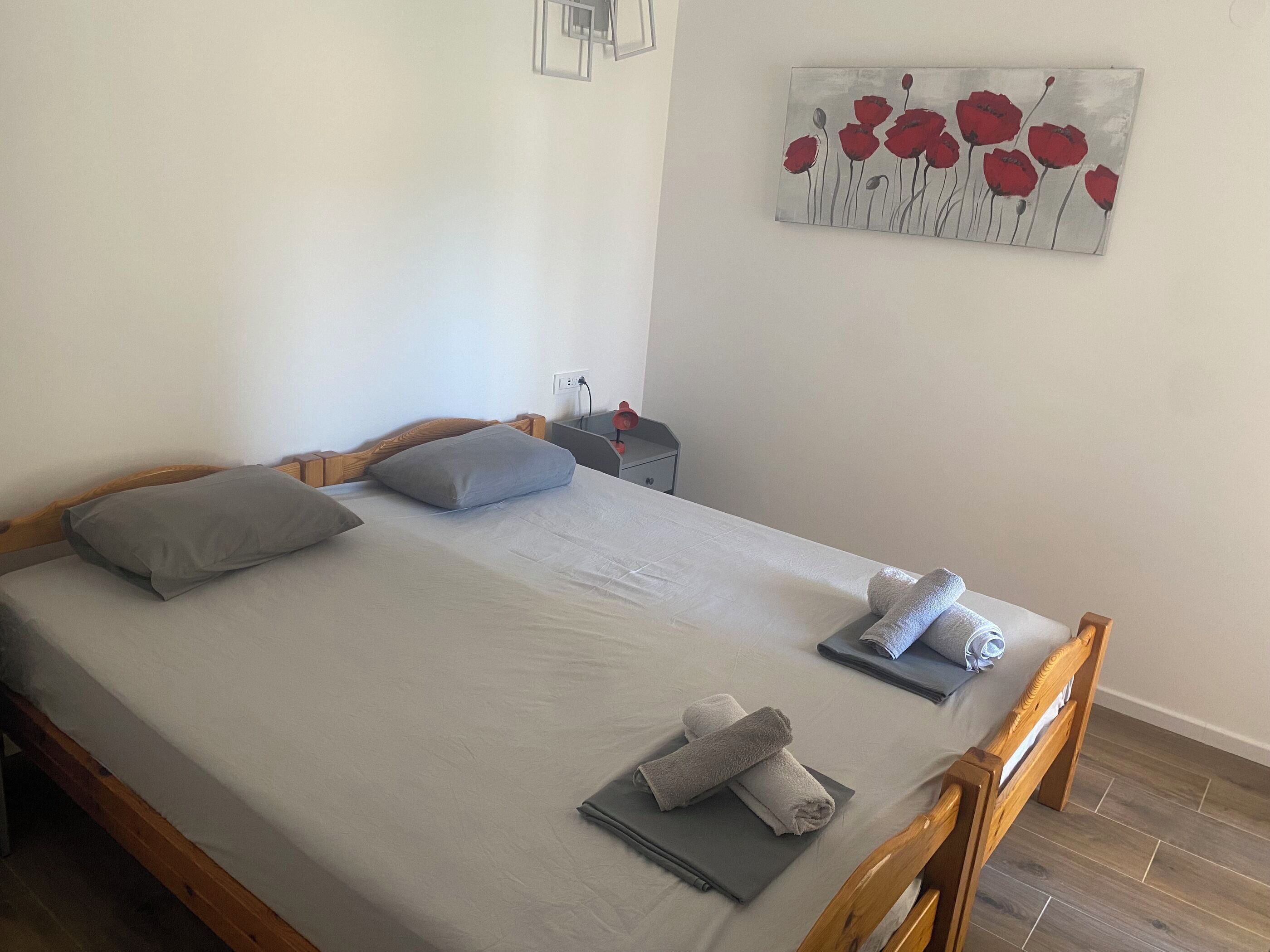 Een opgemaakt bed met kussens, een nachtkastje met een lamp en een schilderij aan de muur.