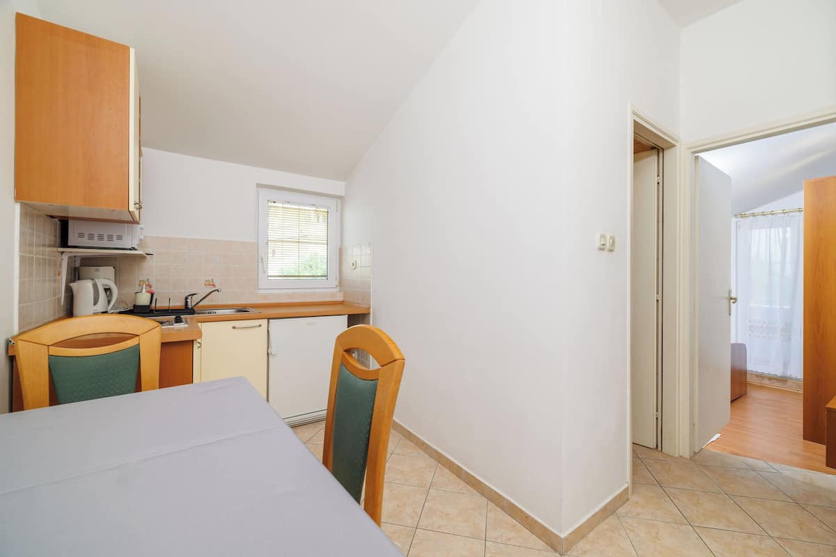 A compact kitchen with wooden cabinets, a small window, and a dining area with a table and chairs.