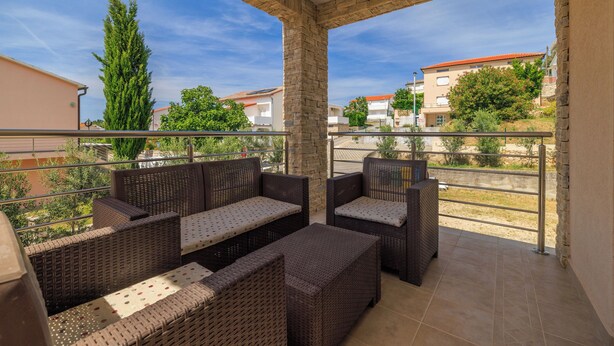 A balcony with wicker furniture, a stone pillar, and a view of the neighborhood. - Apartments Paradise (Lopar)