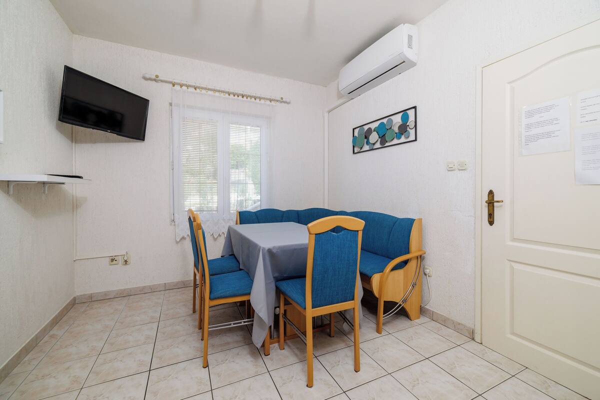 A small, clean room with a dining table, two chairs, a TV, and a door with a notice.