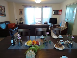 A living room with a sofa, dining table, chairs, a TV, and a window with curtains. - Apartments Rita (Lovran)