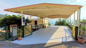 A covered outdoor area with a concrete floor, green metal railing, and potted plants. - Apartments Rita (Lovran)