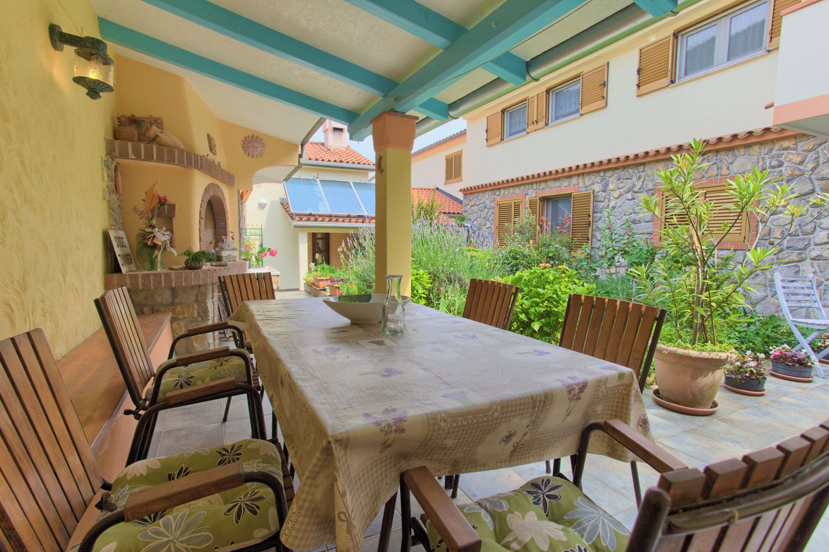 A covered patio with a table and chairs, surrounded by potted plants and a stone wall.