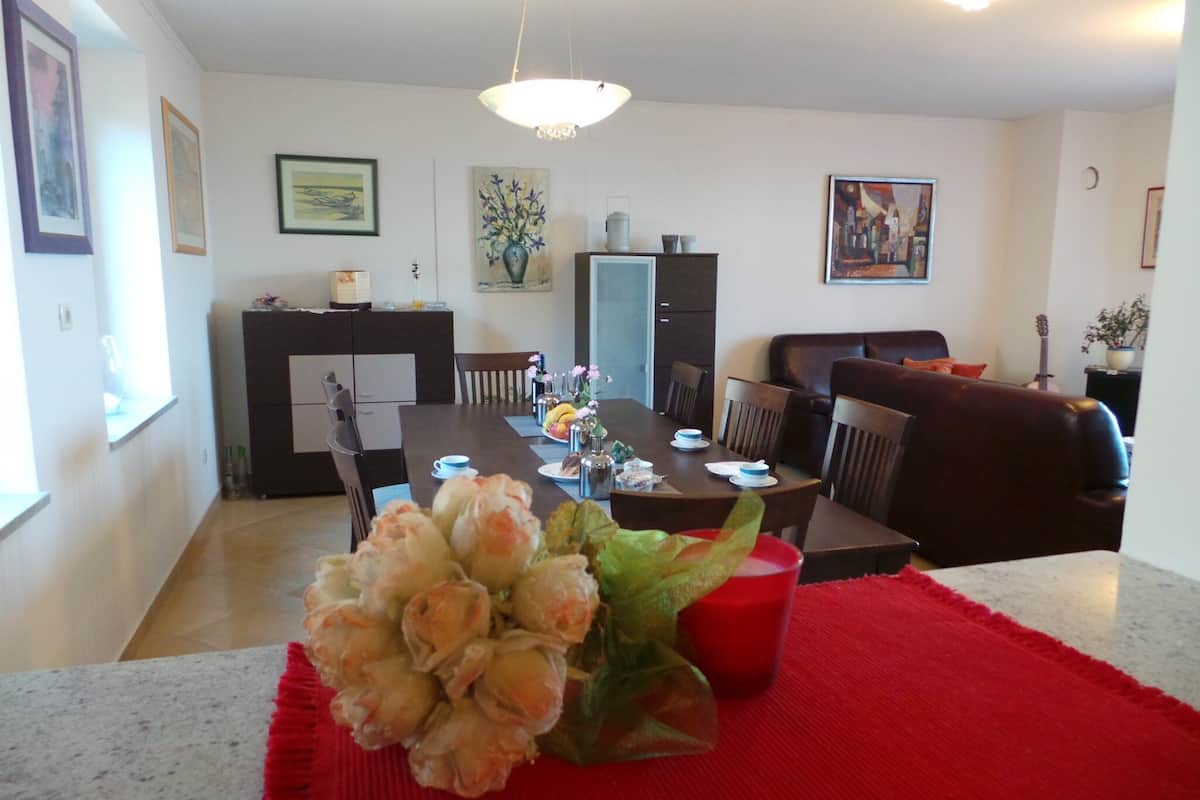 Un comedor con una mesa dispuesta para cuatro personas, rodeada de sillas. Hay una servilleta roja sobre la mesa y un jarrón con flores en el centro.