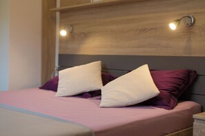 Una cama con cabecera de madera, dos almohadas y una colcha rosa.