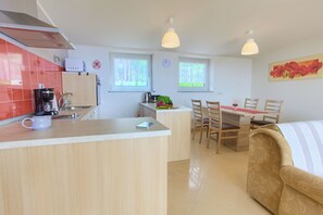 Una cocina moderna con cafetera, hervidor y microondas. Hay un comedor con mesa y sillas, y un sofá.