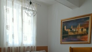 A living room with a sofa, armchair, and ottoman, a painting on the wall, and a geometric-patterned rug. - Apartments Boris i Snjezana (Rab)