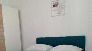 A bed with white bedding and a teal headboard in a room with white walls. - Apartments Boris i Snjezana (Rab)