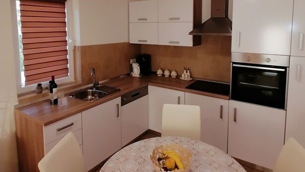 A compact kitchen with white cabinets, a built-in oven, and a dining area with a lace tablecloth. - Apartments Boris i Snjezana (Rab)