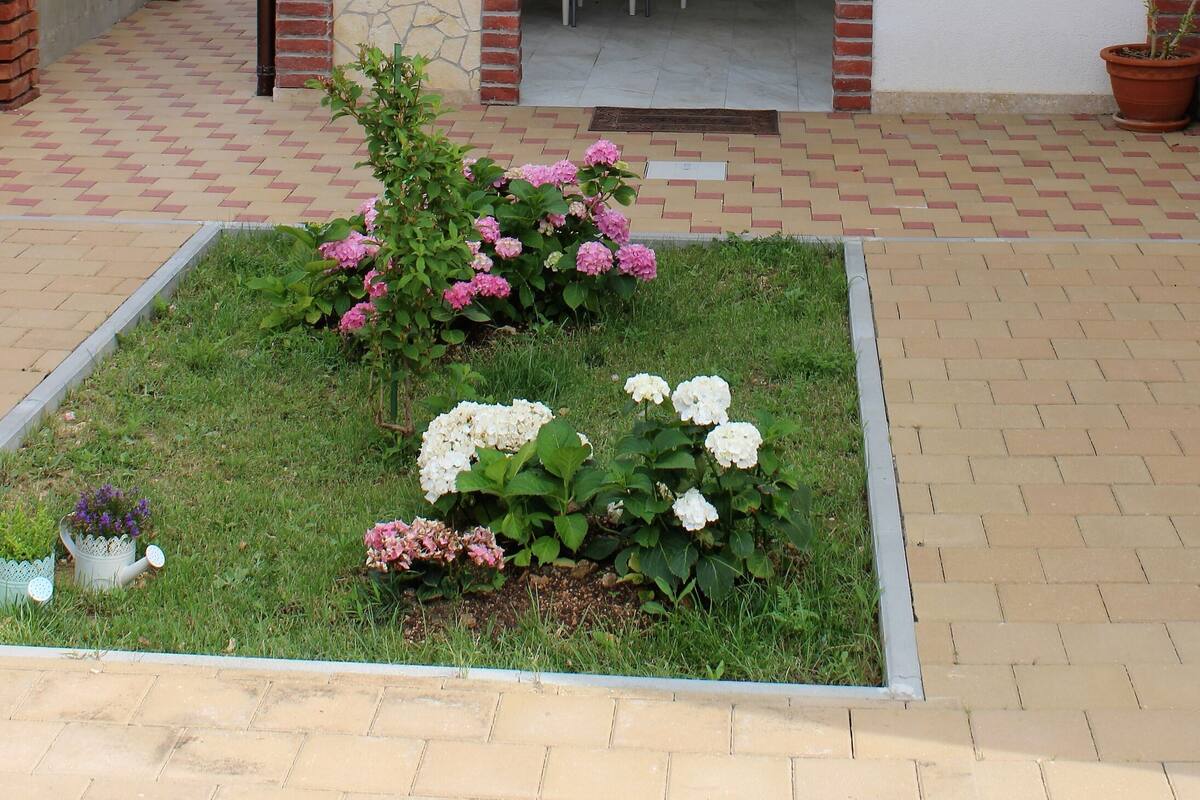 Un portico coperto con tavolo e sedie, un piccolo giardino fiorito e un muro in mattoni.