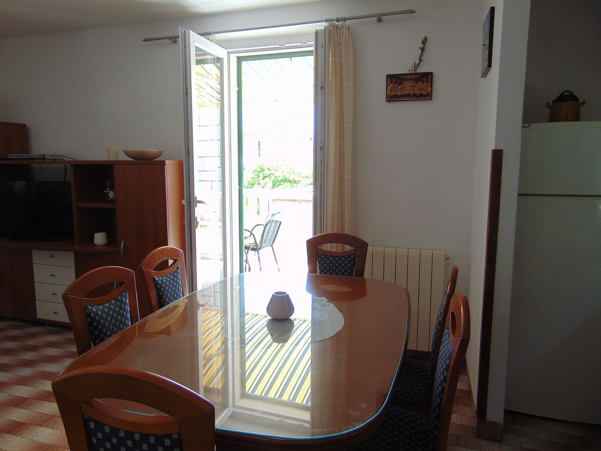 Un comedor con mesa de vidrio, cuatro sillas, un armario de madera y un radiador.