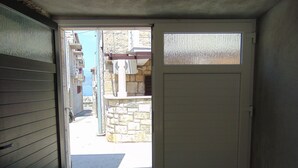 A doorway leading to a courtyard with a stone wall and a building in the background. - Apartment Fran (Postira)
