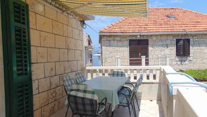 An outdoor patio with a table and chairs, a striped awning, and a stone building with shutters in the background. - Apartment Fran (Postira)