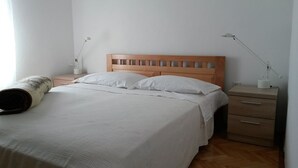 A bedroom with a wooden headboard, a bed with white bedding, a bedside table with a lamp, and a wooden nightstand. - Apartments Janja (Solta)