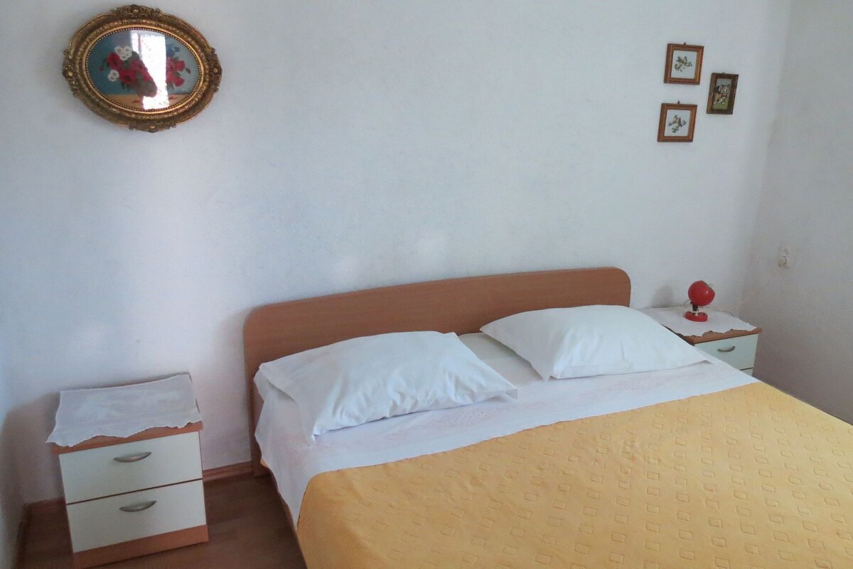 A simple bedroom with a bed, a nightstand, a dresser, and a mirror on the wall.